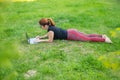 Woman is shopping on a laptop while lying on her stomach on green grass in a park. A student with two glasses is