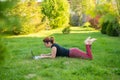 Woman is shopping on a laptop while lying on her stomach on green grass in a park. A student with two glasses is