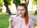 Young caucasian woman stay in park and show white credit card with black magnet line. Shopping and retail concept Royalty Free Stock Photo