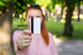 Young caucasian woman stay in park and show white credit card with black magnet line. Shopping and retail concept Royalty Free Stock Photo