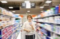 Woman with shopping list pushing cart looking at goods in supermarket Royalty Free Stock Photo