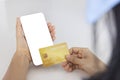 A woman shopping online on her sofa at home with a smartphone using a gold credit card. And use your credit card to tap the screen Royalty Free Stock Photo