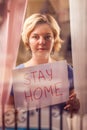 Woman staying in flat in front of window holding a sheet of paper with title stay home. People and healthcare concept