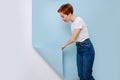 Woman with short ginger hair pulling piece of blue covering from a white wall