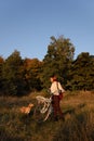 Woman with short hair stands in the autumn forest with bicycle, looking at her English cocker spaniel dog during sunset. Royalty Free Stock Photo