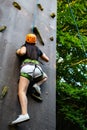 Woman in shorts and black shirt with safety equipment climbing