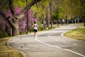 Woman in shorts with hair up running on curved paved running path through park in springtime with redbud tree in bloom