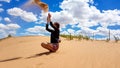 Xilinhot - A woman in shorts throwing sand above her head while sitting on a sand dune on Hunshandake Desert