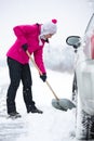 Woman shoveling snow around the car