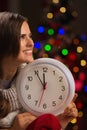 Woman showing clock in front of Christmas lights