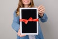 Woman showing digital tablet with red ribbon gift isolated on grey background pad pda modern technology people person concept free Royalty Free Stock Photo