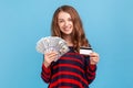 Woman showing fan of dollars and plastic credit card, choosing proper way of payments. Royalty Free Stock Photo