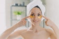 Woman showing golden moisturizing hydrogel patches on under eye skin in bathroom. Skincare routine