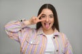 Happy woman showing her tongue and V-sign on gray background Royalty Free Stock Photo