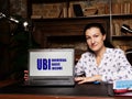 Woman showing laptop computer with UBI UNIVERSAL BASIC INCOME icon on screen background, success in business concept