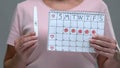 Woman showing pregnancy test and period calendar at camera, pregnancy attempt