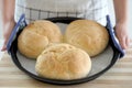 Woman showing three homemade loaves of bread in baking tray freshly baked