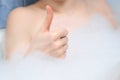 Woman is showing thumb up sign lying in bath with foam, closeup view.
