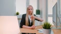 Woman showing thumbs down in office. Sitting at workplace young blond female in business suit looking at camera and Royalty Free Stock Photo