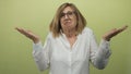 Woman shrugging in studio setting against green backdrop with raised hands and puzzled expression; uncertainty Royalty Free Stock Photo