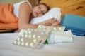 Woman is sick in bed. The lady lies in bed with pills. Sick adult girl. Home medicine treatment