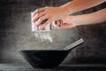Woman sifting flour with sieve in black bowl