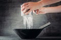 Woman sifting flour with sieve over black bowl on dark background Royalty Free Stock Photo