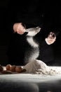 woman sifts flour through sieve onto table with eggs on black background.