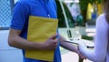 Woman signing proof delivery form and receiving yellow package from courier