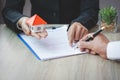 A woman signs a contract to purchase a home with a real estate agent. Model house in hand Royalty Free Stock Photo