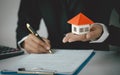 A woman signs a contract to purchase a home with a real estate agent. Model house on hand