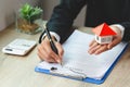 A woman signs a contract to purchase a home with a real estate agent. Model house with keys on table Royalty Free Stock Photo