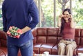 Woman  siiting on couch in living room , pretending to cry and looking at her boyfriend who hiding gift box behind Royalty Free Stock Photo