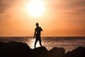 Woman silhouette on the beach in orange sunset standing in rockrs with the sun over the head Royalty Free Stock Photo