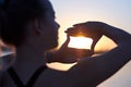 Woman silhouette framing sun with fingers at sunset. Hand shape of a camera across the sky