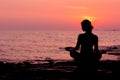 Woman silhouette sitting in lotus position on sea background back lit