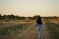 A woman in simple rural clothes and with long black disheveled hair walks through a slanted field from behind view