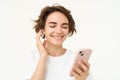 Woman singing along, listening music in wireless headphones, holding smartphone in hand, standing over white background Royalty Free Stock Photo