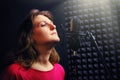 Woman sings into a recording studio on black background. Professional female vocalists in red clothes. Recording singer at a