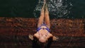 Woman sit on a pier in sunglasses and swimming suit. Girl rest on a flood wood underwater pier. Lady in the water and