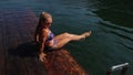 Woman sit on a pier in sunglasses and swimming suit. Girl rest on a flood wood underwater pier. Lady in the water and