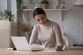 Woman sit at table with laptop jotting information on paper Royalty Free Stock Photo