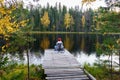 Young woman sit on dock enjoying landscape of autumn forest, lake with colored yellow golden trees Royalty Free Stock Photo