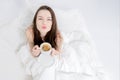 A woman sits in bed and drinks aromatic coffee, looks up, sending a kiss. Tasty breakfast. The brunette is holding a cup. Royalty Free Stock Photo