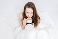 A woman sits in bed and takes a sip of aromatic coffee. Tasty breakfast. The brunette is holding a cup with a hot drink. White Royalty Free Stock Photo