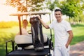 A woman sits behind the wheel of a golf cart, a man stands in the foreground and holds a bag with golf clubs Royalty Free Stock Photo