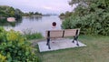 A woman sits on a bench by a lake overlooking Toronto
