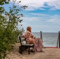 A woman sits on a bench by the sea and looks into the distance.