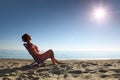 Woman sits on chair on sea-shore by person to sun Royalty Free Stock Photo