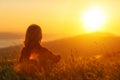 Woman sits with her back in the field and admires the sunset in mountains Royalty Free Stock Photo